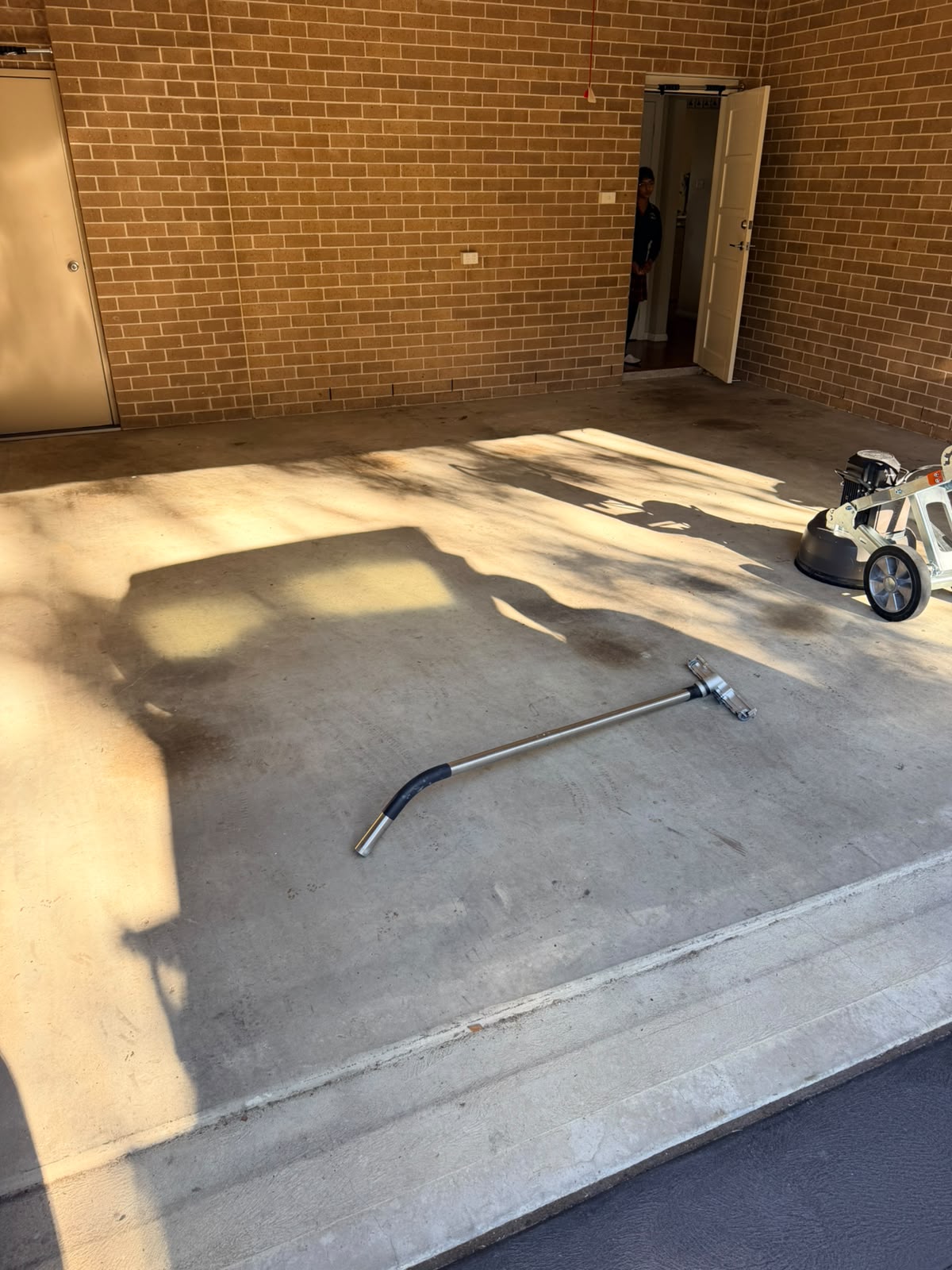Bare concrete garage slab before epoxy coating, with the grinder at the side