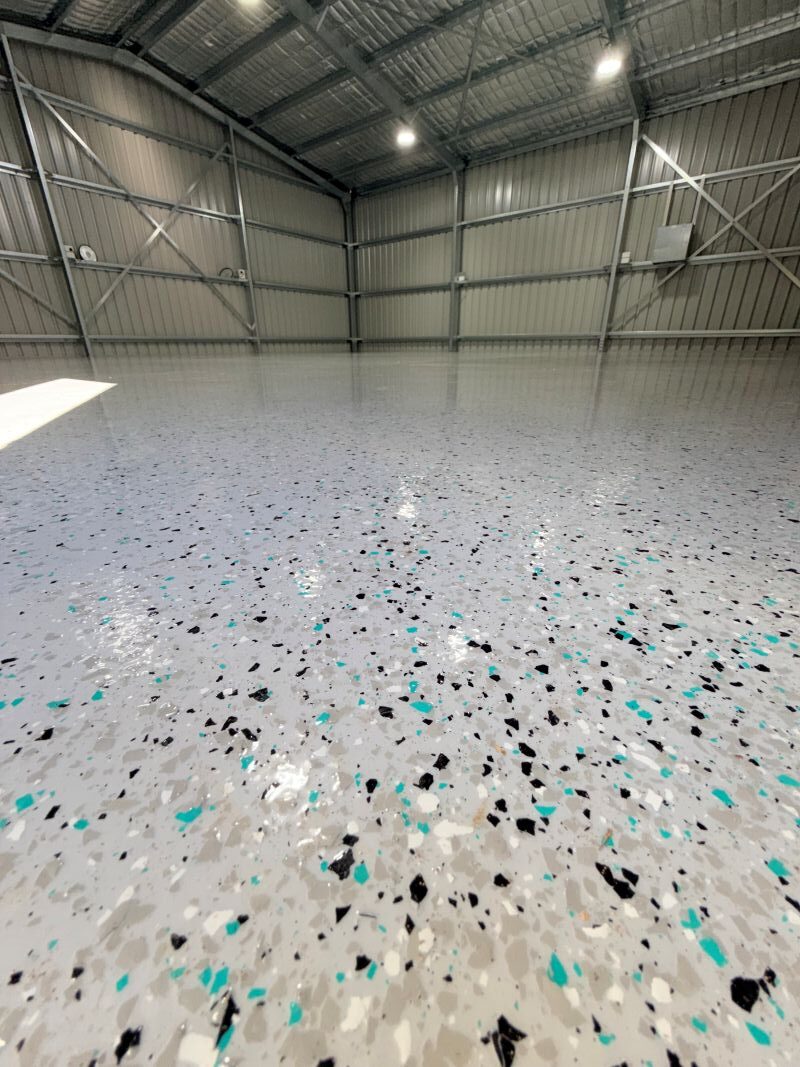 Teal flake broadcast over a light grey epoxy base in a shed